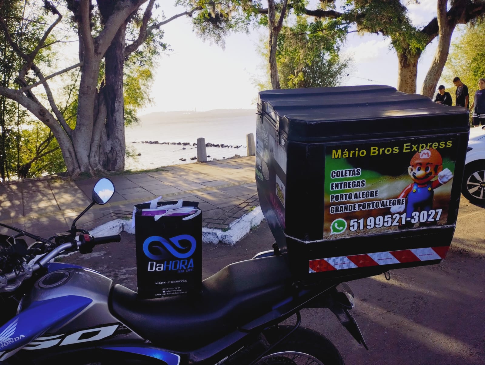 Motocicleta com baú adesivado estacionada na orla de Porto Alegre
